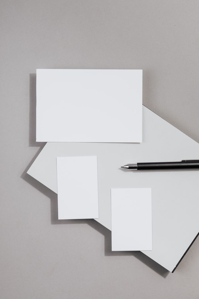 Top view of blank business cards and pen on a gray surface.